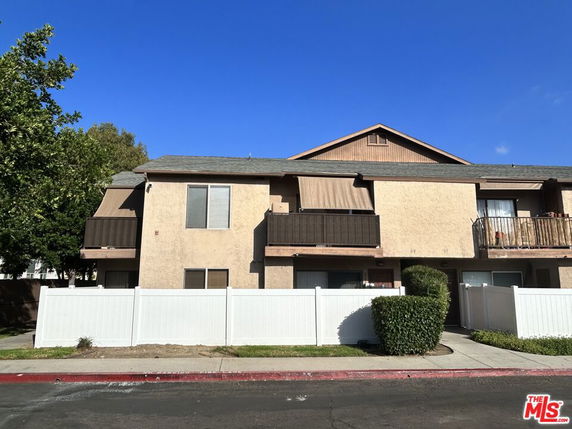 Front view of a two-story residential building with balconies and a white fence.