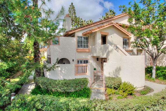 Front view of a two-story house with a light stucco exterior and brown roof tiles.