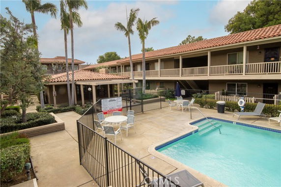 Outdoor swimming pool area surrounded by a two-story building with palm trees.