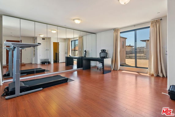 Room with a treadmill, mirror wall, and desk.