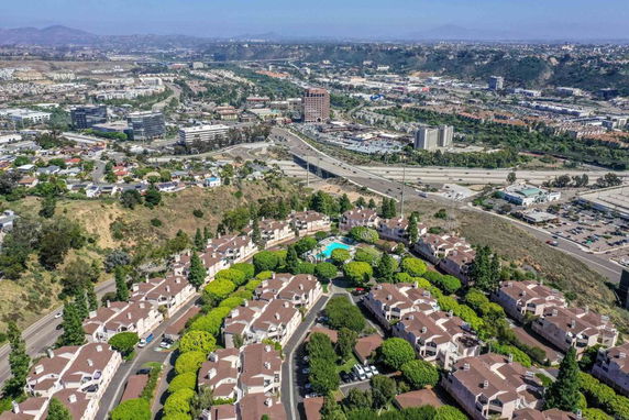 Panoramic view of residential complex with multiple buildings and a swimming pool, overlooking roads and a cityscape in the distance.