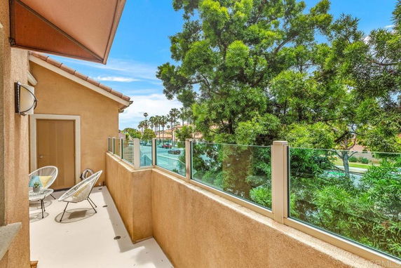 View from a balcony with glass railing overlooking trees and a distant street.