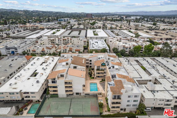 Aerial view of a residential complex with multiple buildings, swimming pool, and surrounding cityscape.