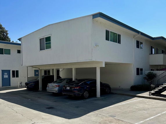 Outdoor parking area with cars parked under a building.