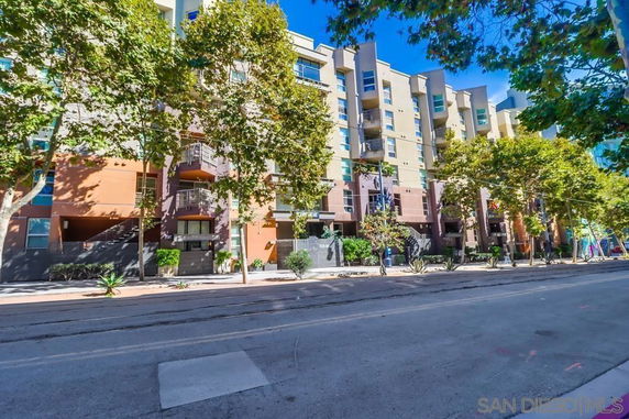 Front view of a multi-story residential building with balconies and trees lining the sidewalk.