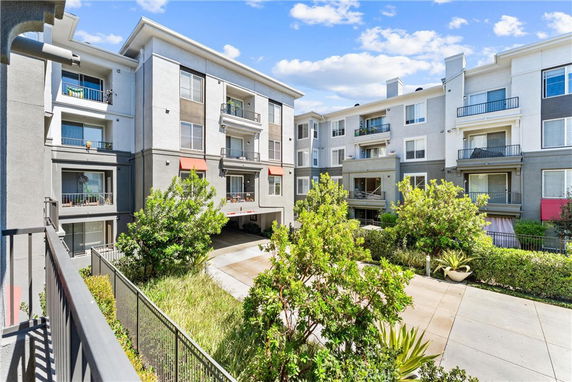 Front view of a multi-story residential building with multiple balconies and a driveway entrance.