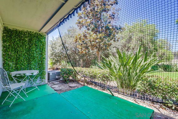 Outdoor area with a small table and chairs next to a green wall and netting, overlooking a garden.