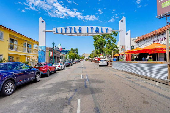 Street view with a sign reading 'Little Italy' above, lined with cars and restaurants.