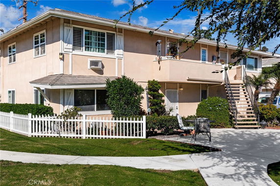 Front view of a two-story house with an external staircase and white picket fence.