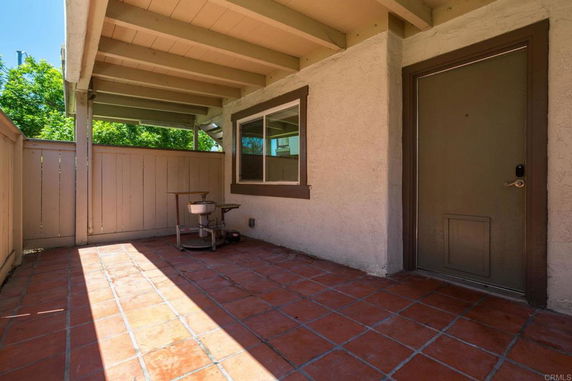 Covered outdoor area with tiled flooring, a window, and a door.