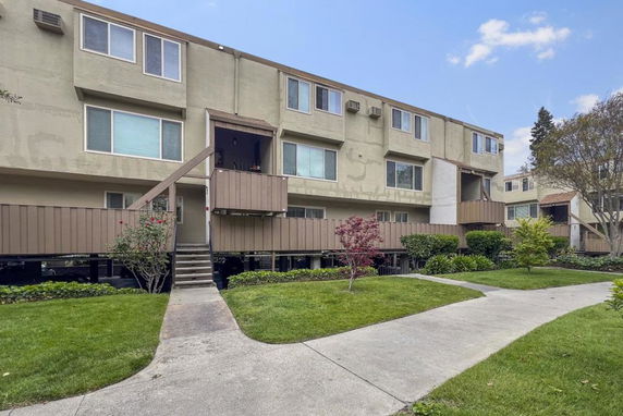 Front view of a multi-story apartment building with balconies and stairs leading to the main entrance.