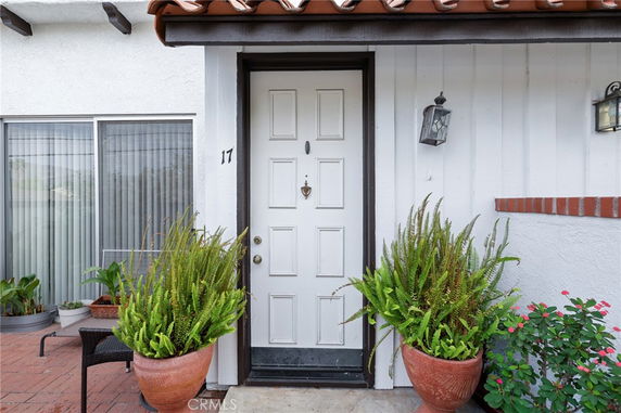 Front entry of a house with a white door, plants in pots, and decorative lamps.