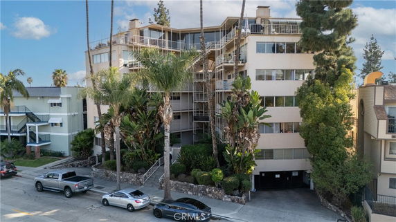 Front view of a multi-story apartment building with balconies and palm trees.