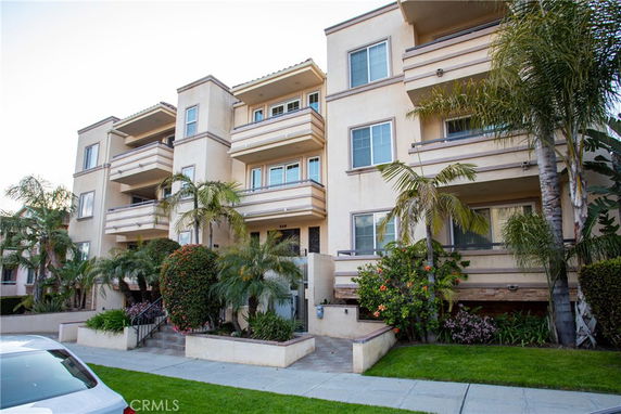 Front view of a multi-story residential building with balconies and palm trees.