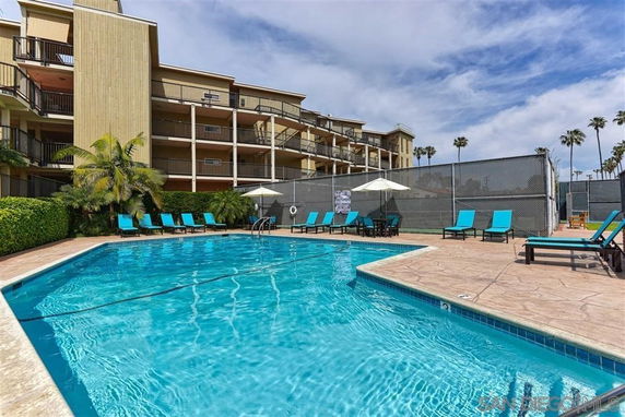 Outdoor swimming pool area with lounge chairs and umbrellas next to a multi-story building.