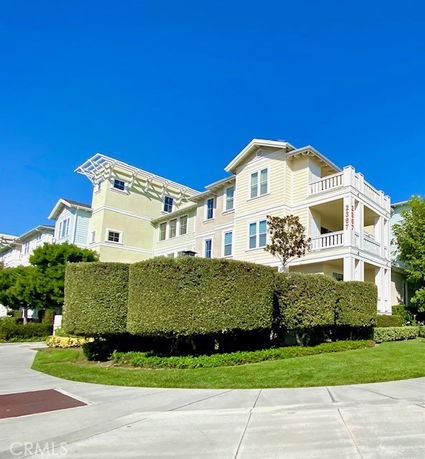 Front view of a three-story residential building with balconies and well-maintained hedges.
