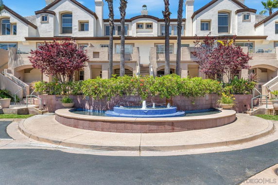 Front view of a multi-story residential building with landscaped entrance and a water fountain.