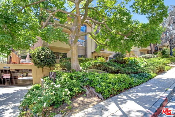 Front view of a multi-story residential building with surrounding greenery and sidewalk.
