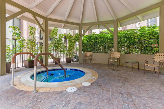 Outdoor hot tub under a covered pavilion with seating and greenery around.