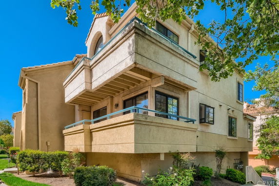 Front view of a multi-story house with balconies and beige stucco exterior.