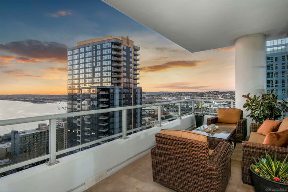 Panoramic view from a balcony overlooking a cityscape and waterfront at sunset.