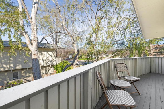 View from a balcony with two chairs, overlooking trees and a neighboring building.