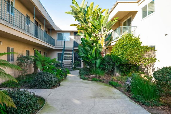 Outdoor view of a two-story residential building with a central pathway and lush greenery.