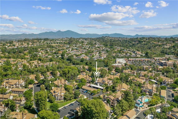 Panoramic view of a residential area with houses and greenery, set against a backdrop of hills and mountains.