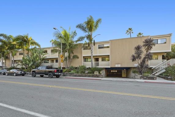 Front view of a multi-story apartment building with surrounding palm trees.