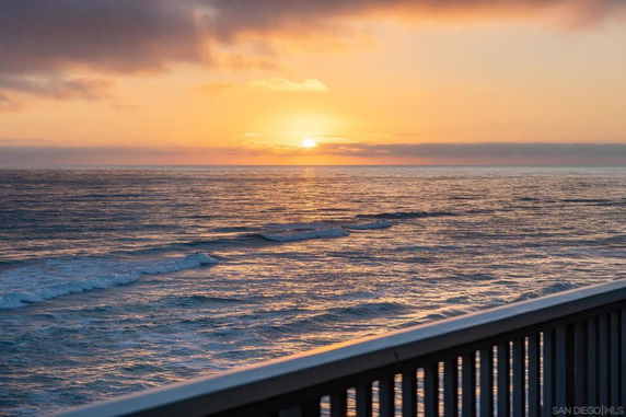 Wide view of ocean with a sunset and railing in the foreground.