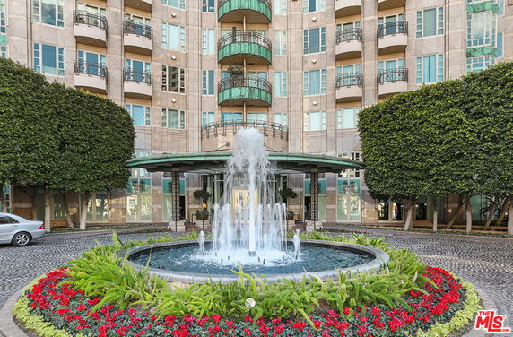 Front view of a multi-story building with balconies and a central water fountain.