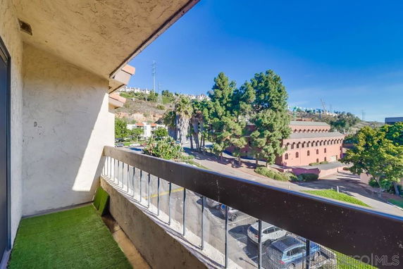 View from a balcony overlooking a street and nearby buildings with trees in the vicinity.