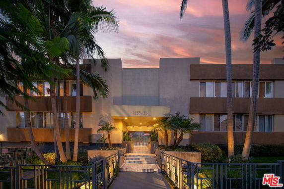 Front view of a multi-story residential building with palm trees and a gated entrance.