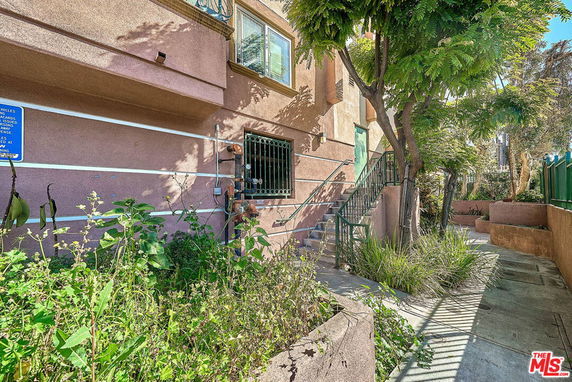 Front view of a multi-story building with exterior staircase and surrounding plants.