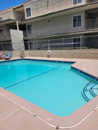 Outdoor swimming pool in front of a multi-story building with balconies.
