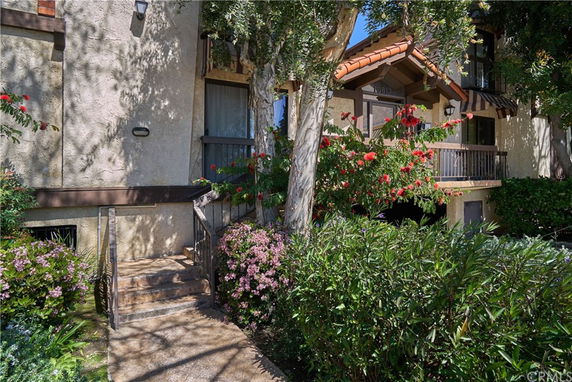 Front view of a residential building with a staircase, plants, and trees.