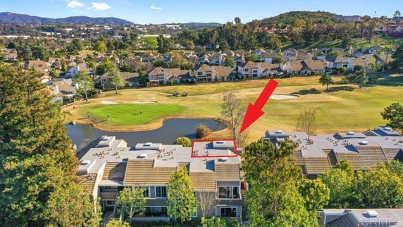 Aerial view of residential buildings near a golf course with hills in the background.