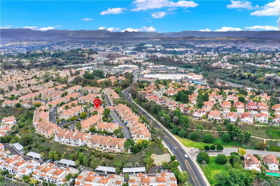Wide aerial view of a residential suburb with houses and roads, surrounded by hills in the distance.