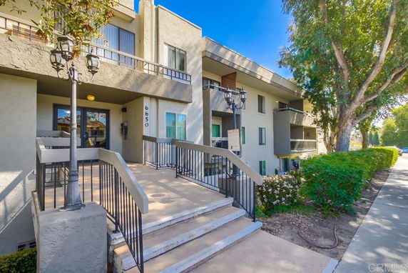 Front view of a two-story residential building with balconies and stairs leading to the entrance.