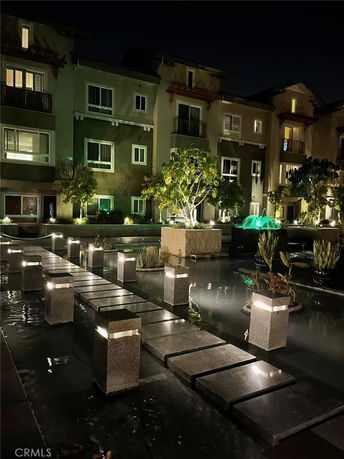 Night view of a multi-story residential building with a stepping stone path and water feature.