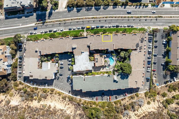 Aerial view of a large building with a flat rooftop, surrounded by parking areas.