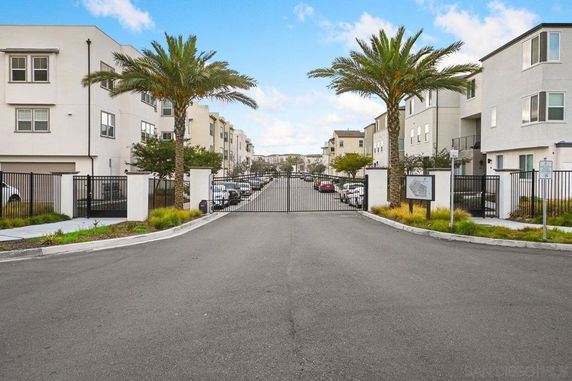 Entrance view of a gated residential complex with parking area and tall palm trees.
