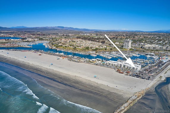 Aerial panoramic view of a coastal area with a wide beach and marina.