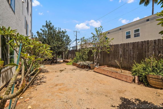 Backyard area with dirt ground, plants, and a wooden fence next to a building.