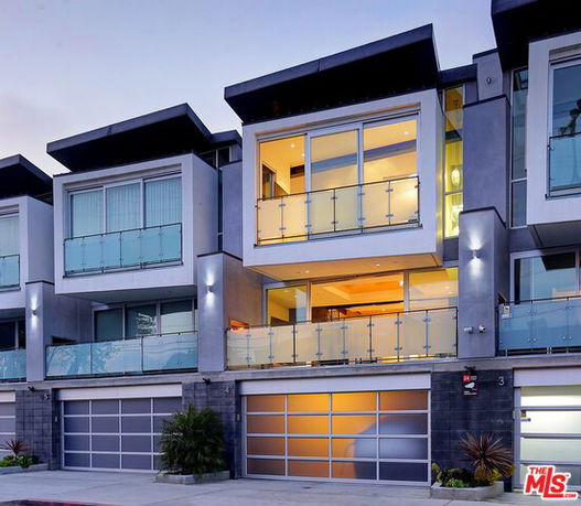 Front view of a modern multi-story residential building with glass balcony railings and large windows.