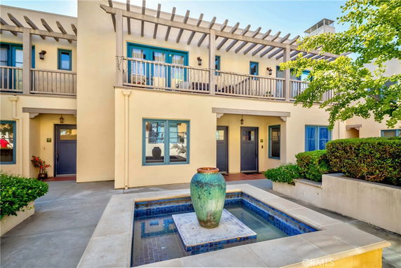 Front view of a residential building with two levels, featuring a balcony with a pergola, windows, and a courtyard with a fountain.