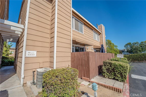 Front view of a multi-story residential building with beige siding, fenced patio, and visible air conditioning unit.