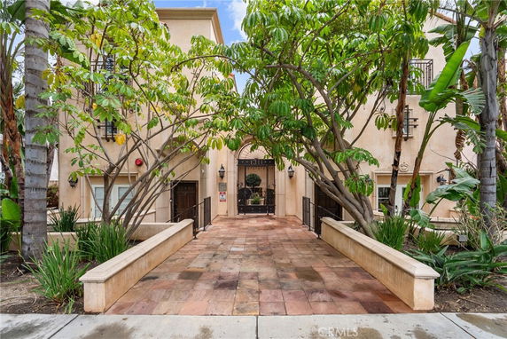 Front view of a multi-story residential building with a pathway lined by trees leading to the entrance.