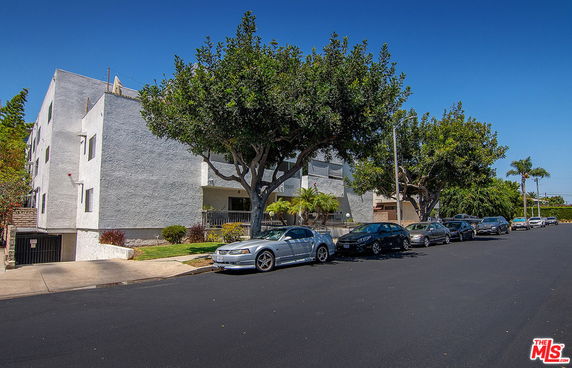 Front view of a multi-story residential building with trees and parked cars