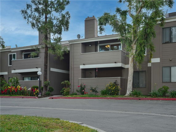 Front view of a multi-story residential building with balconies and surrounding greenery.